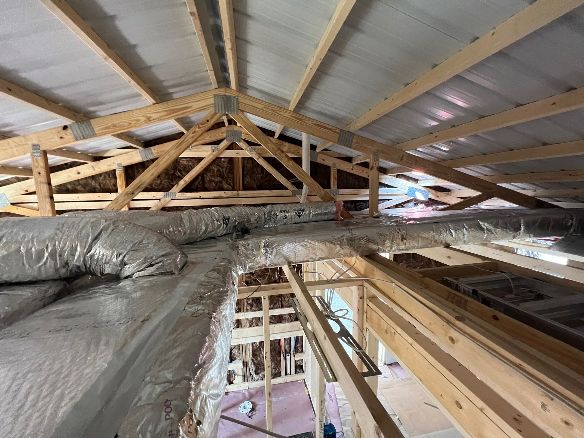 Interior view of a wooden attic structure, insulated with silver foil-wrapped ductwork visible.