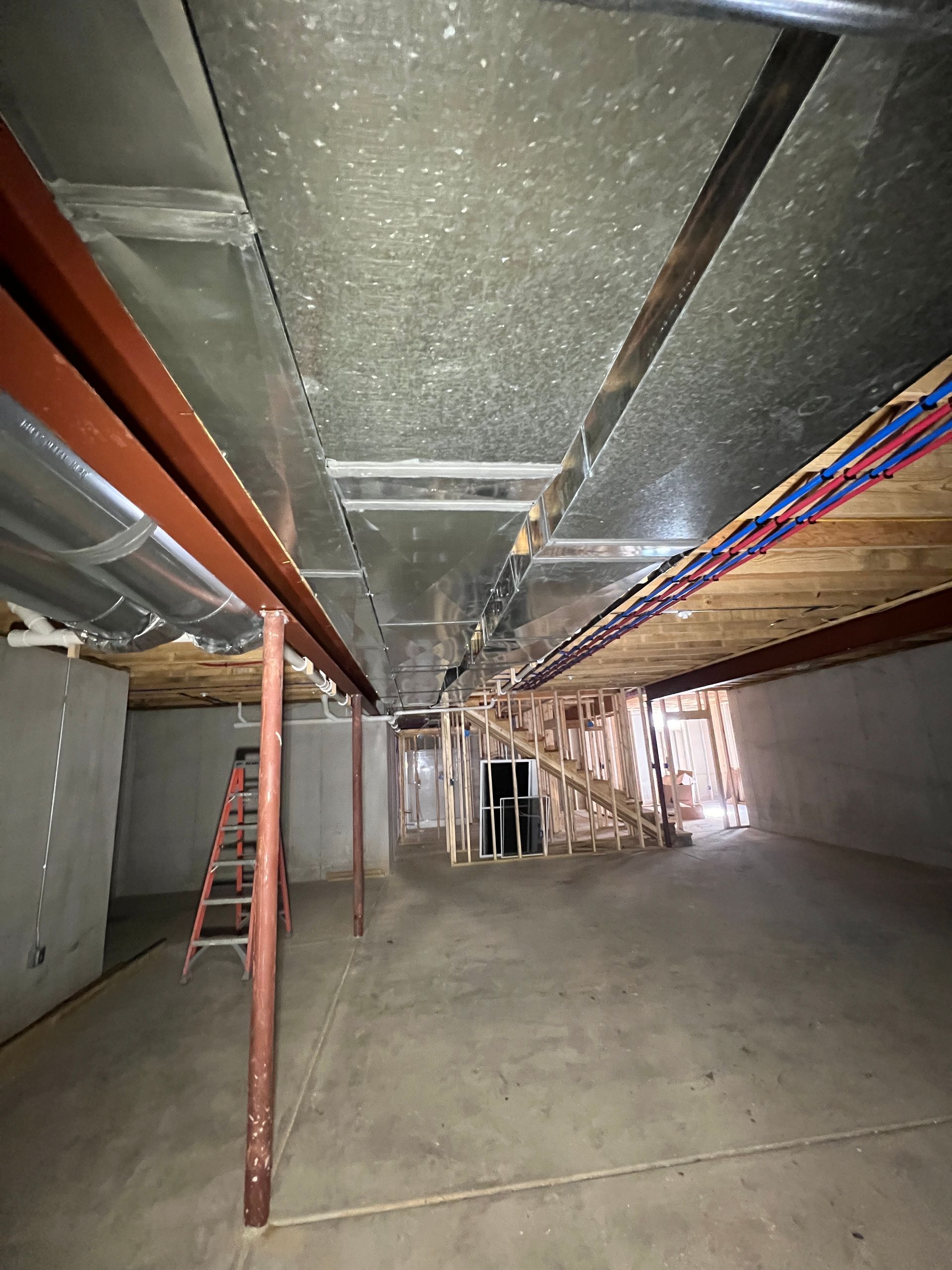 Basement under construction, concrete floor, metal beams, ductwork, unfinished wooden structures, ladder.