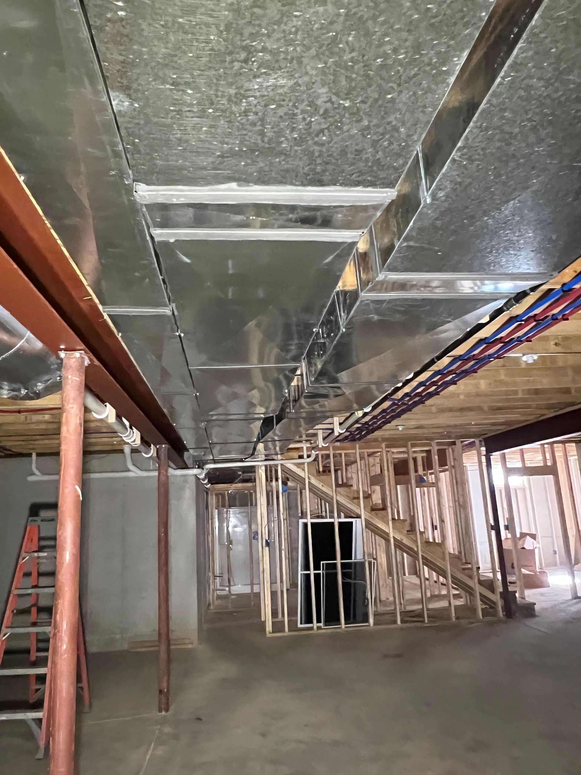 Basement under construction, showing ductwork, exposed framing, and concrete floor.