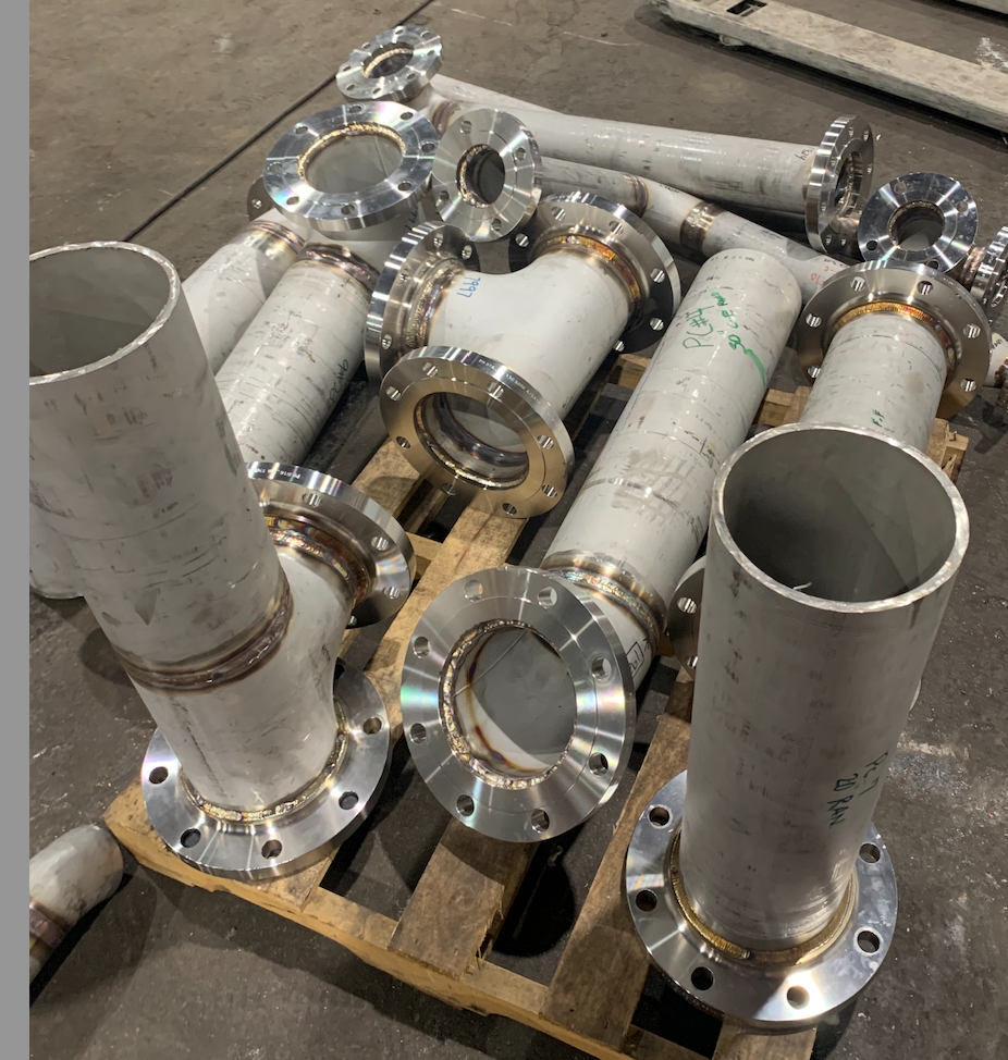 Welded stainless steel pipes and fittings with flanges stacked on a wooden pallet.