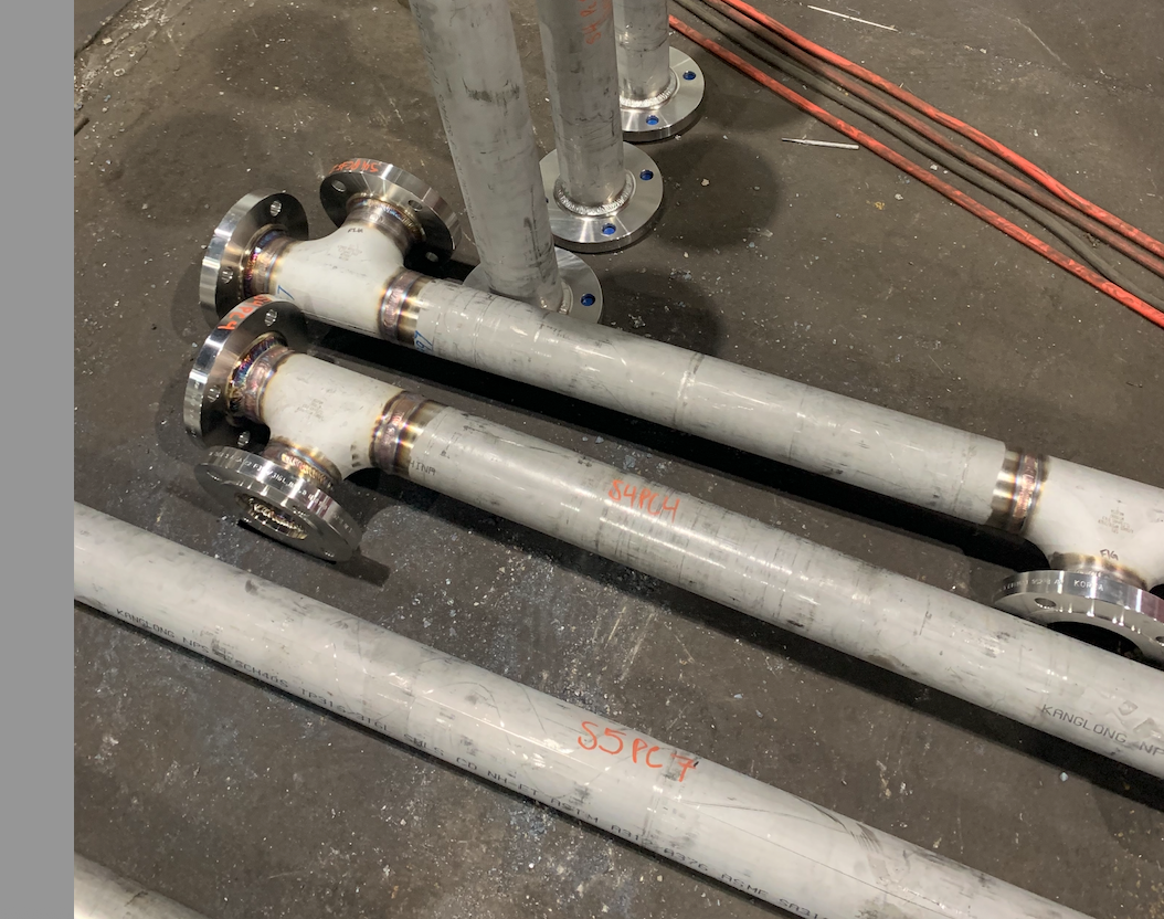 Metal pipes with flanges, welded connections, and tee fittings on a floor.