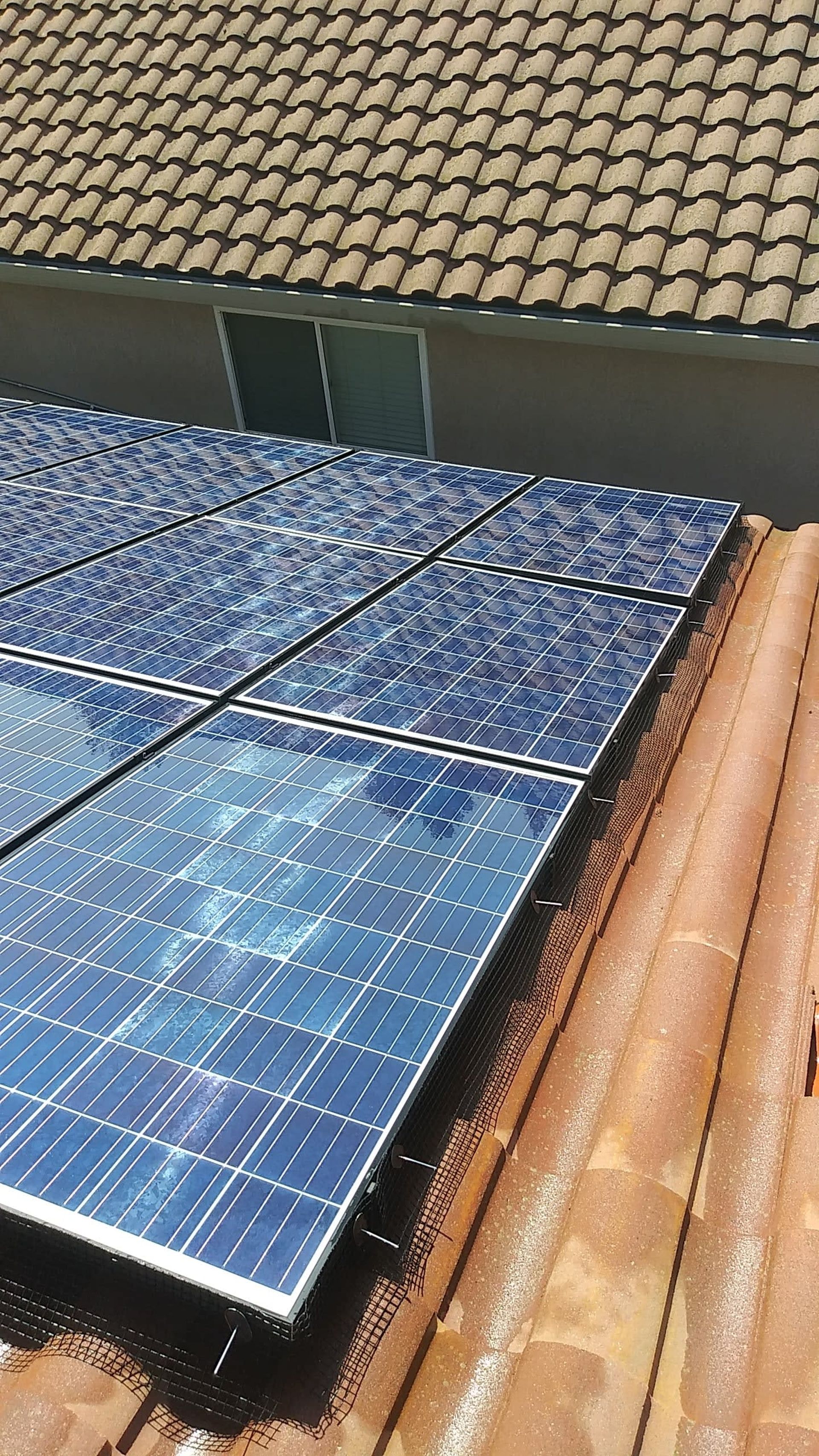 Solar panels installed on a brown tile roof with the top of a building visible in the background.