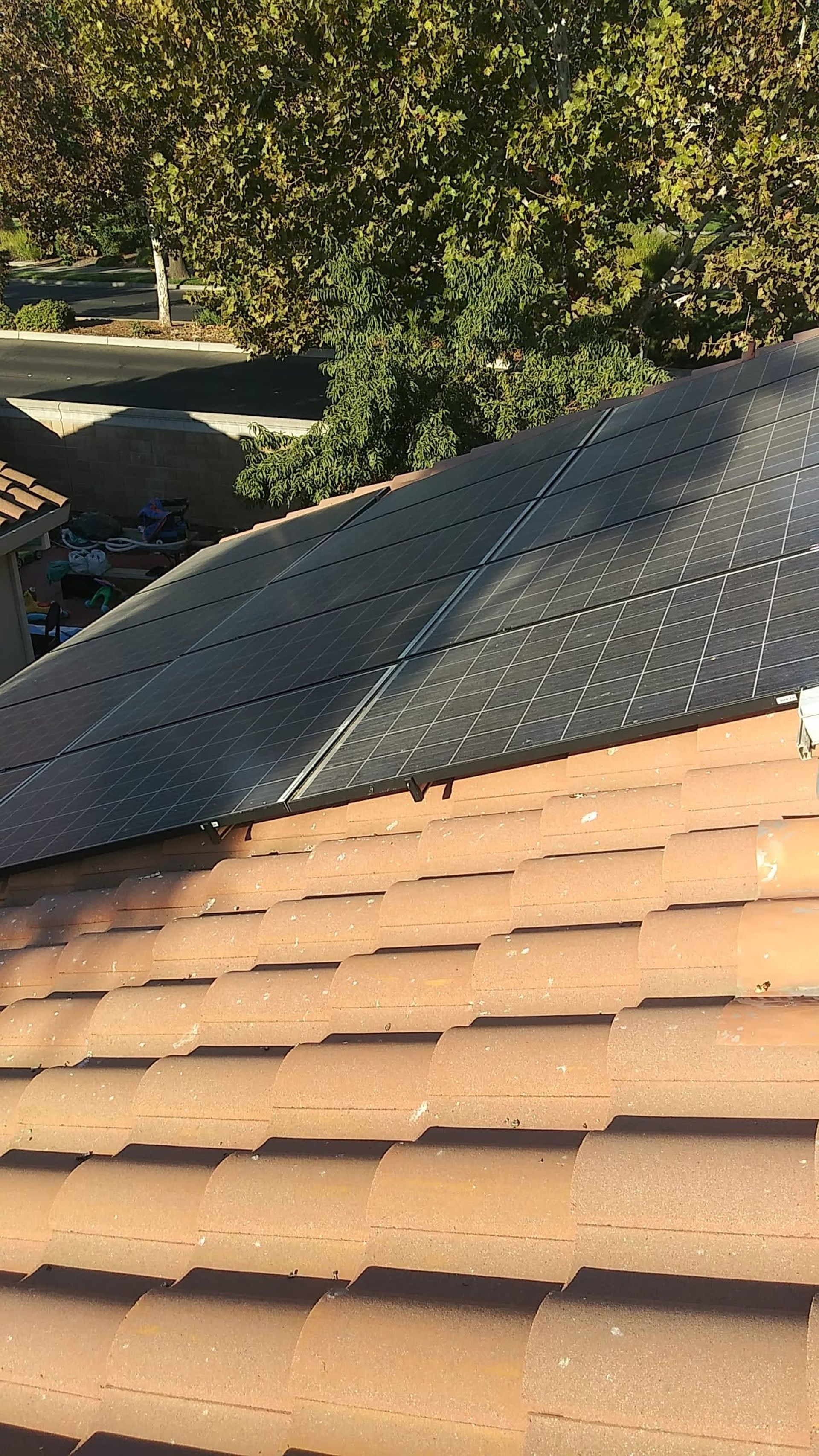 Brown shingle roof with black solar panels. Trees and road visible in the background.