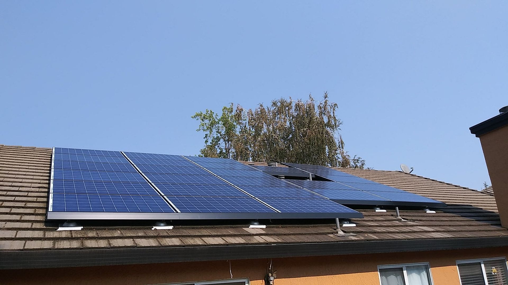 Solar panels installed on a brown-shingled roof under a clear blue sky.
