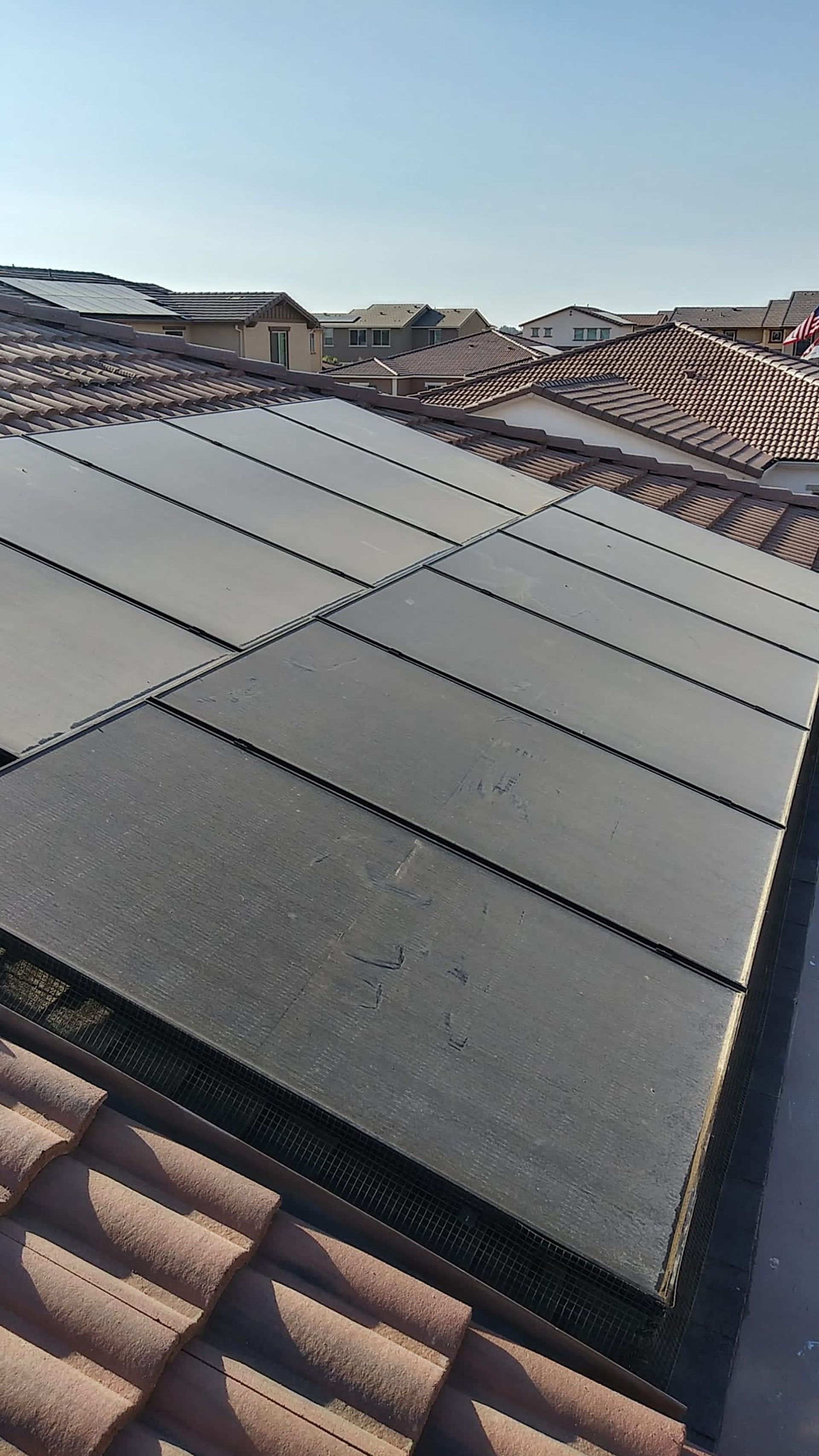 Solar panels installed on a red tile roof, view from above, with houses and sky in the background.