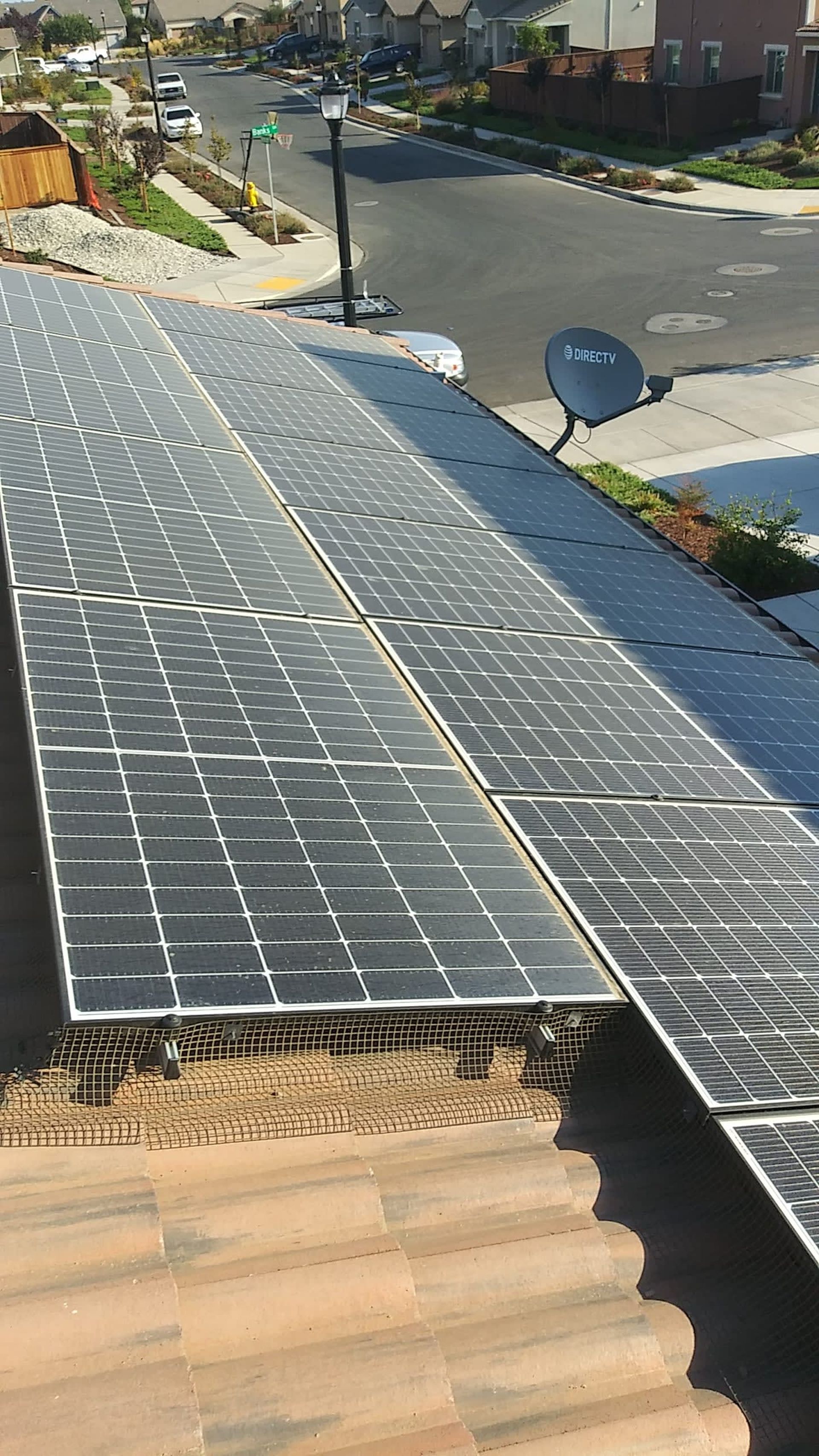 Solar panels on a roof; street and houses in the background.