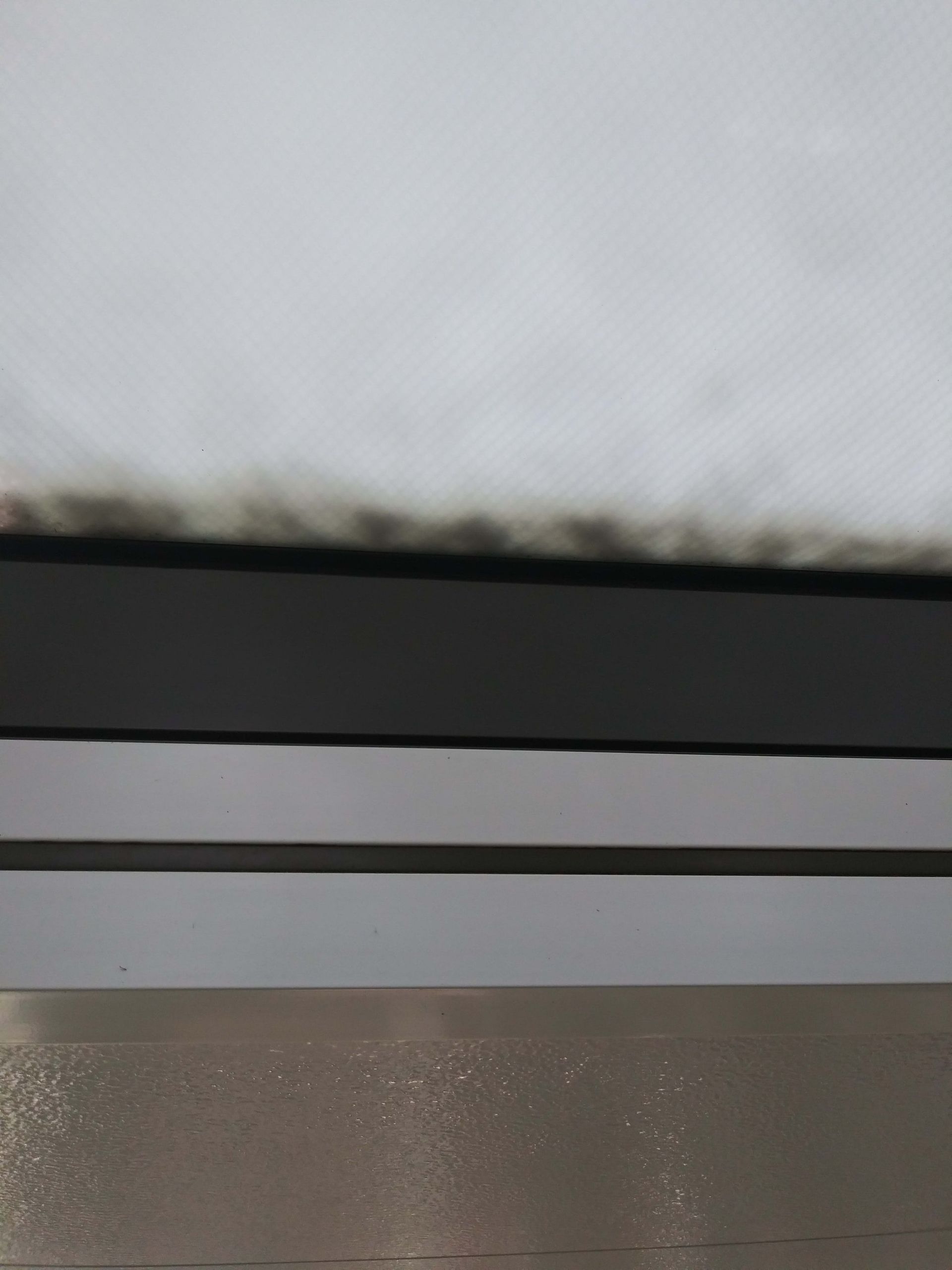 View of a window frame and cloudy sky. Dark top frame, lighter bottom frame, and white sky.