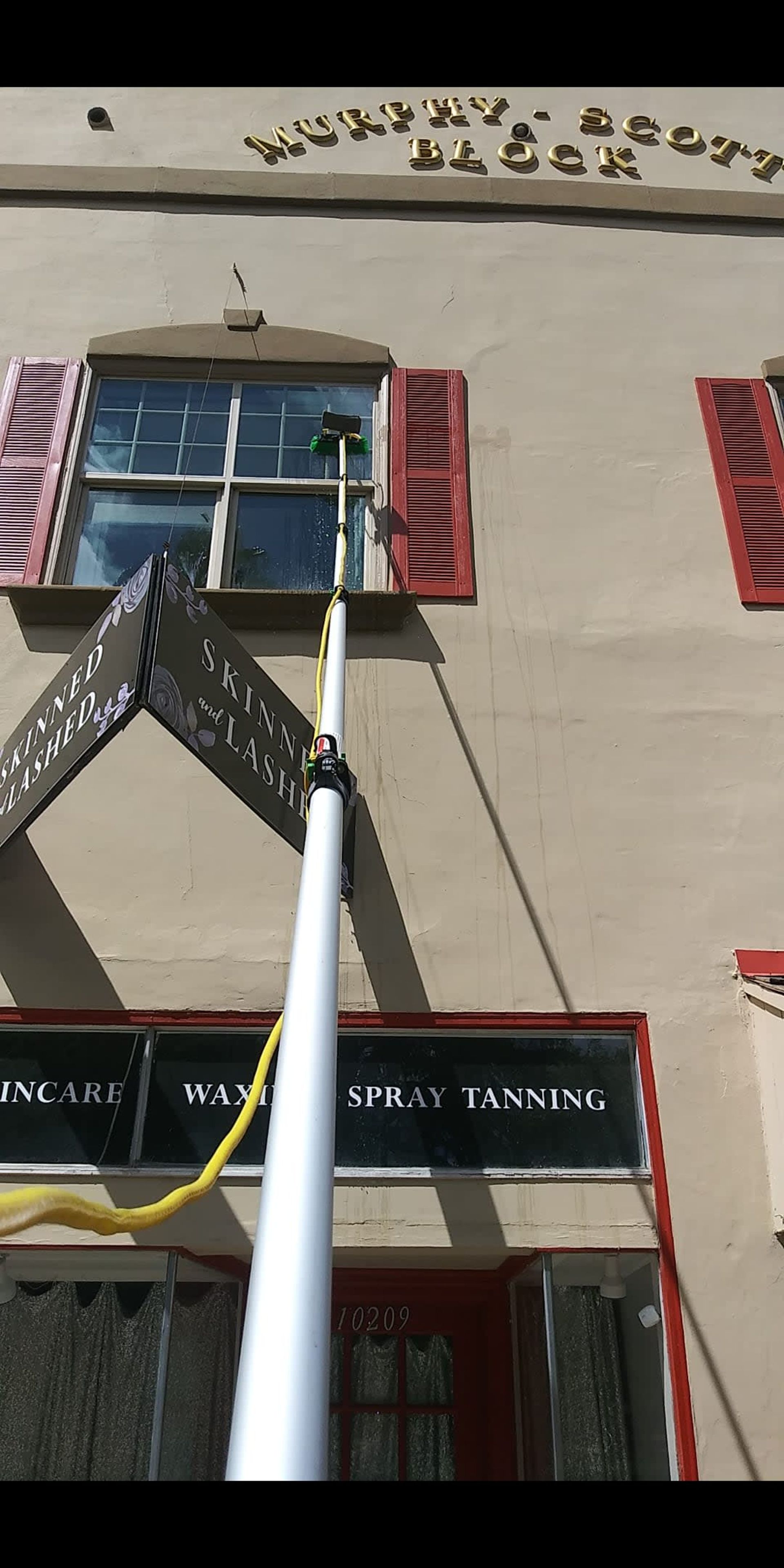 Window cleaner using a pole to wash windows on a building with red shutters.