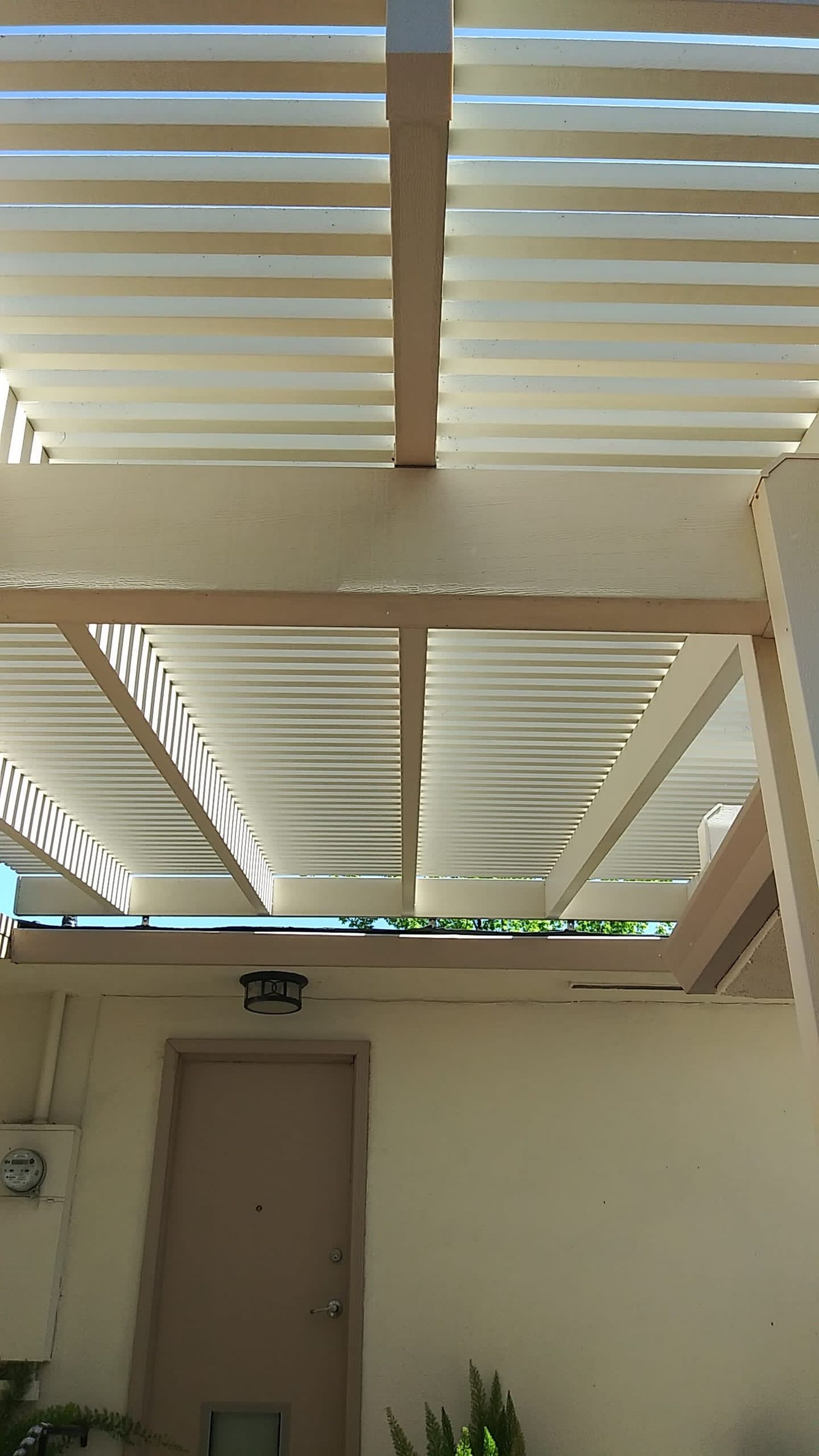 White pergola roof over a beige building with a light beige door.