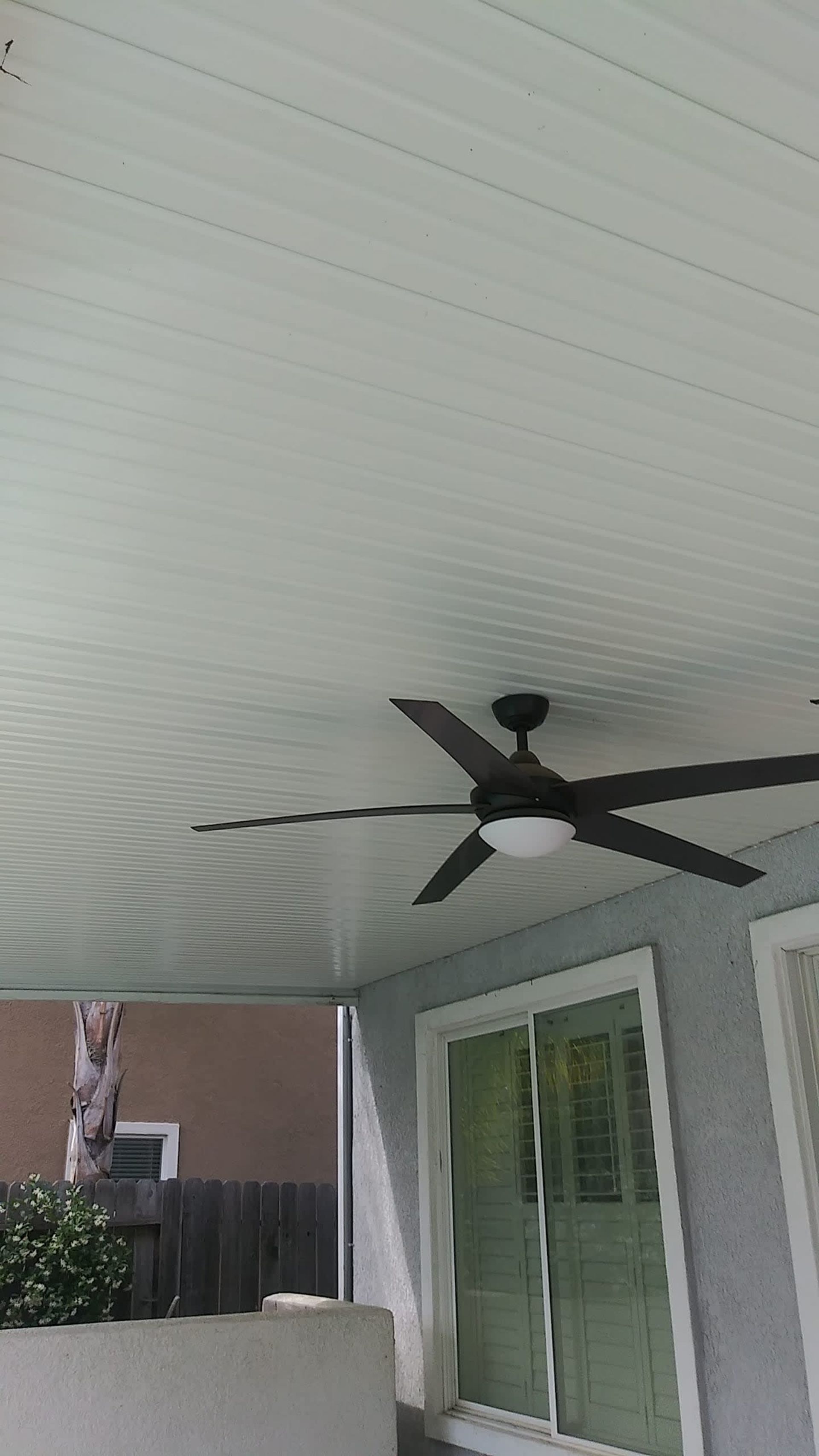 Patio ceiling with fan, sliding glass door, and a glimpse of a tree in the background.