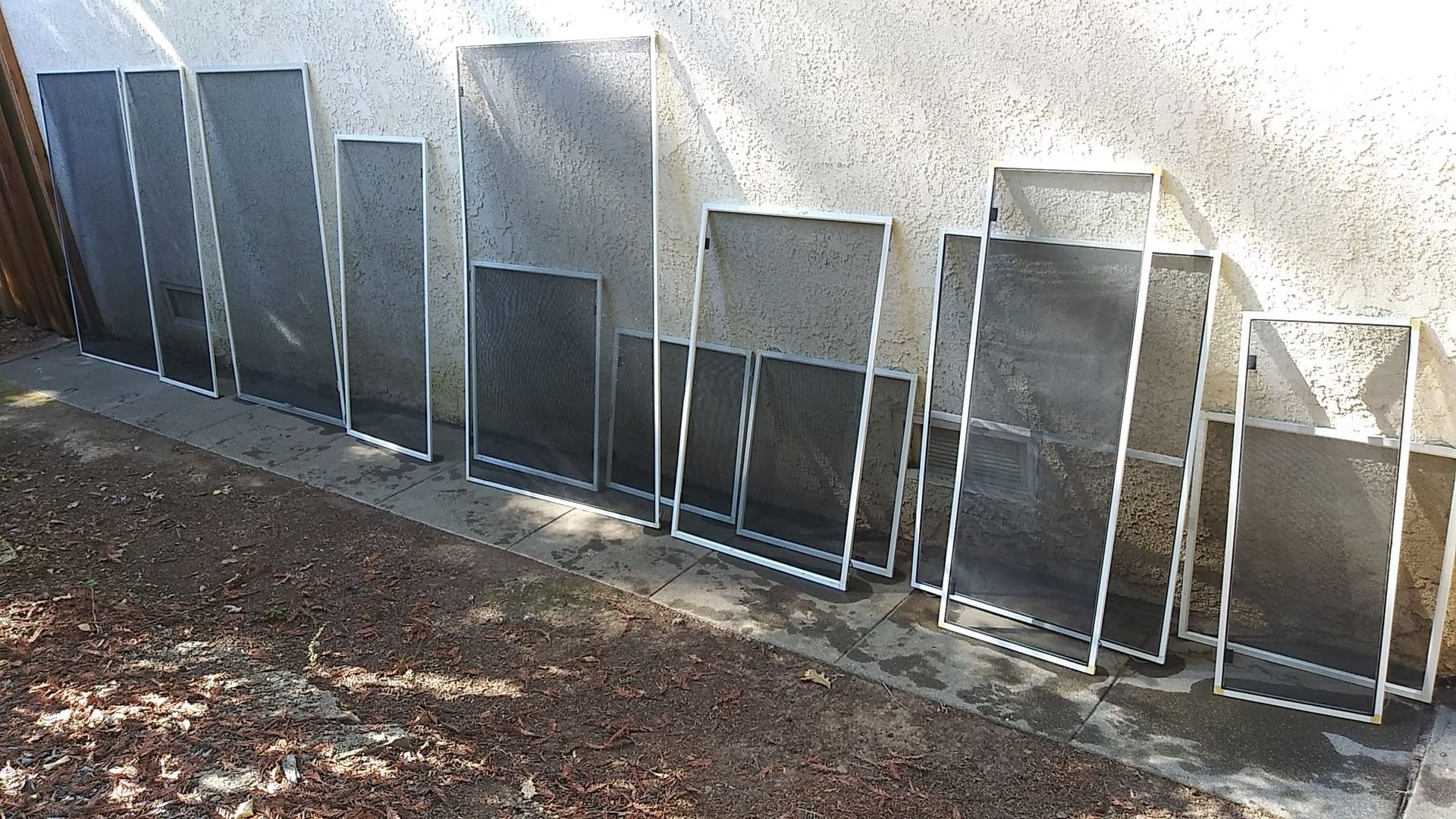A collection of window screens leaning against a wall outside.