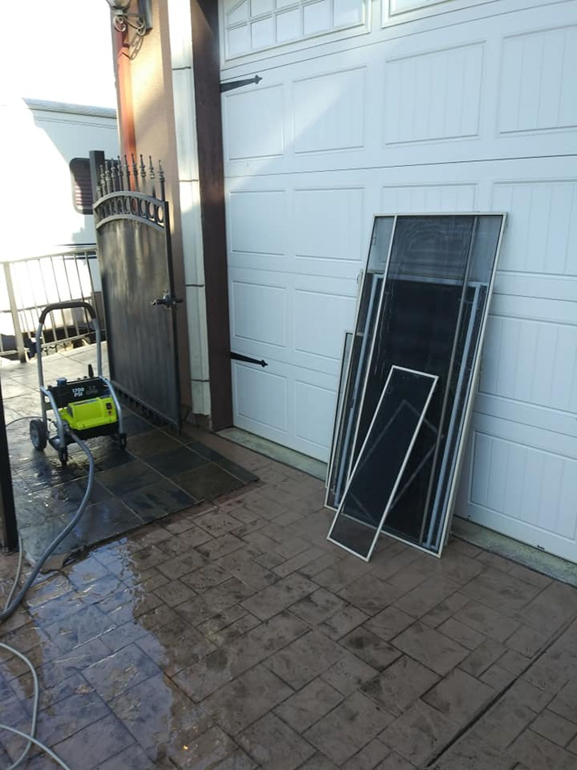 Power washer next to a metal gate and screens leaning against a garage door. 