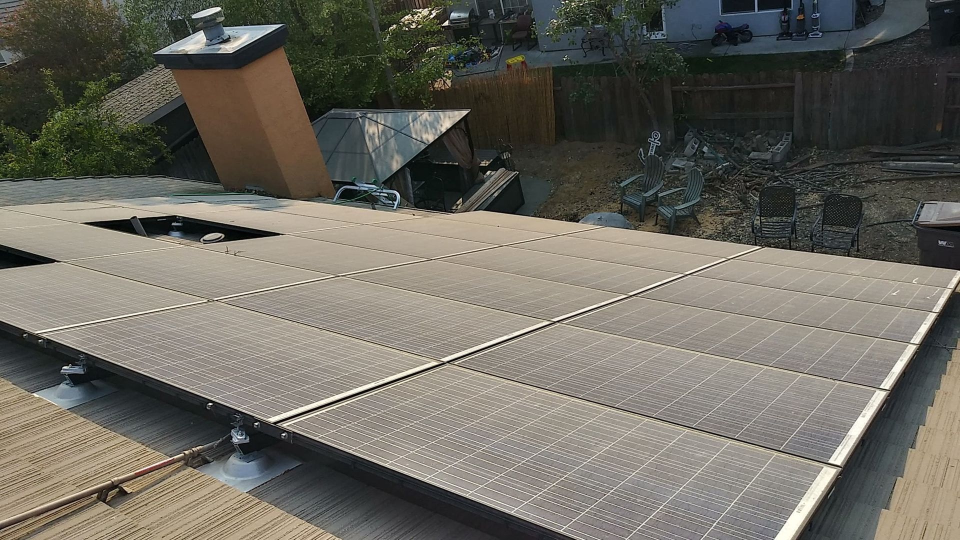 Rooftop with solar panels installed, chimney, and debris. Sunny day.