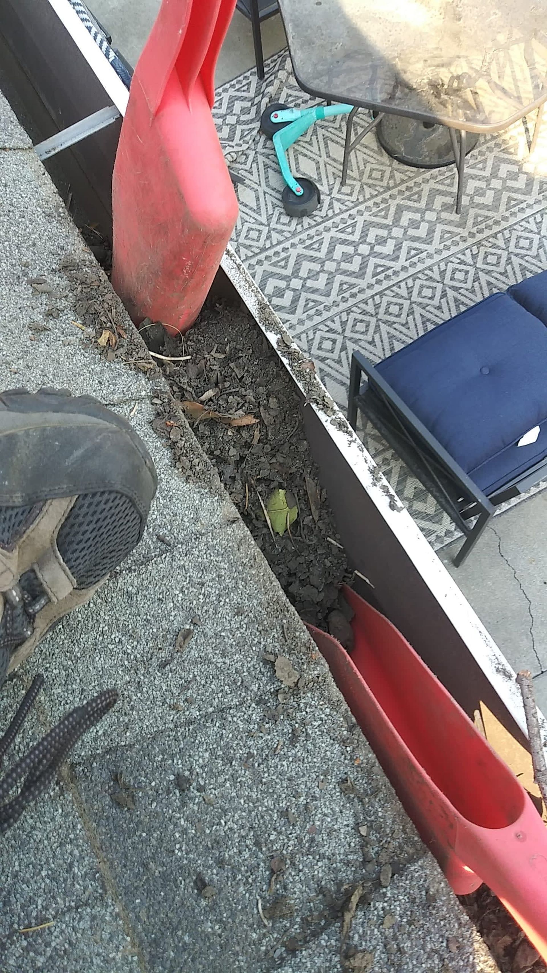 Person cleaning a gutter on a rooftop with a red scoop. 