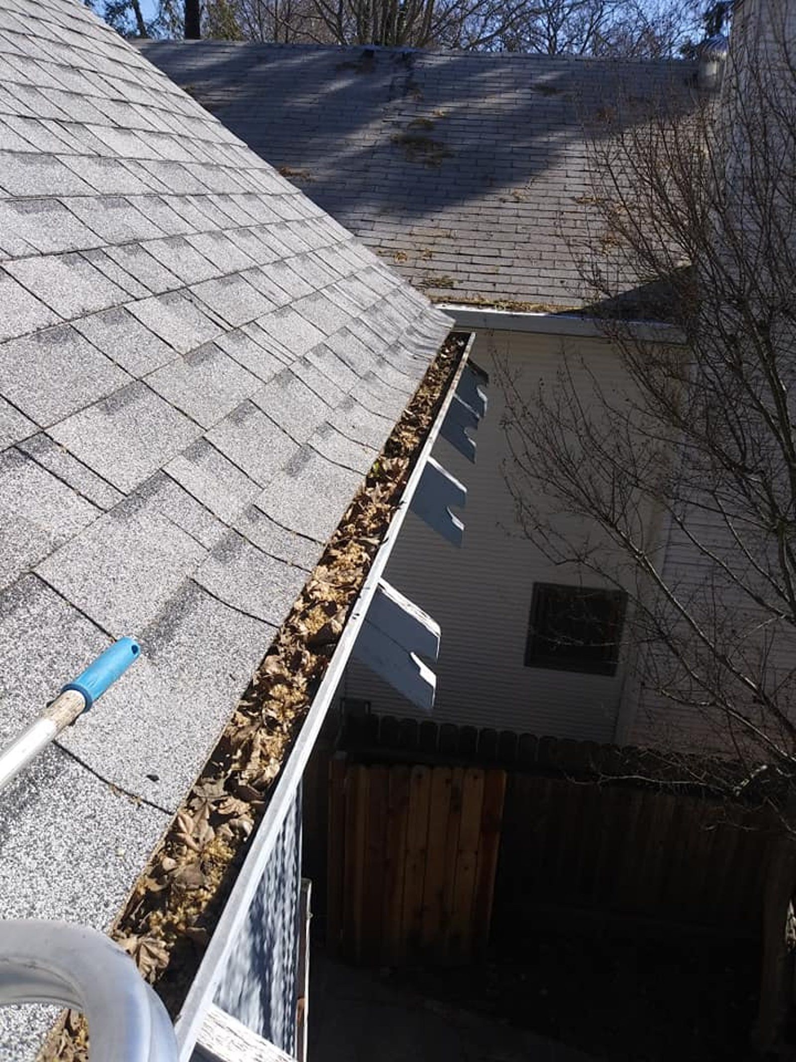 Roof gutter filled with debris being cleaned, daylight outdoors.