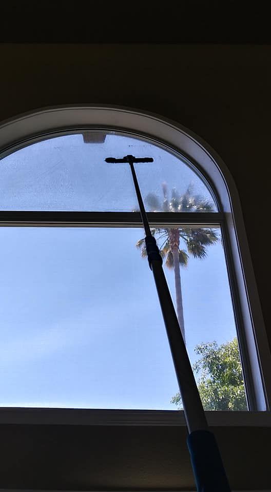A person cleaning an arched window with an extended cleaning tool.