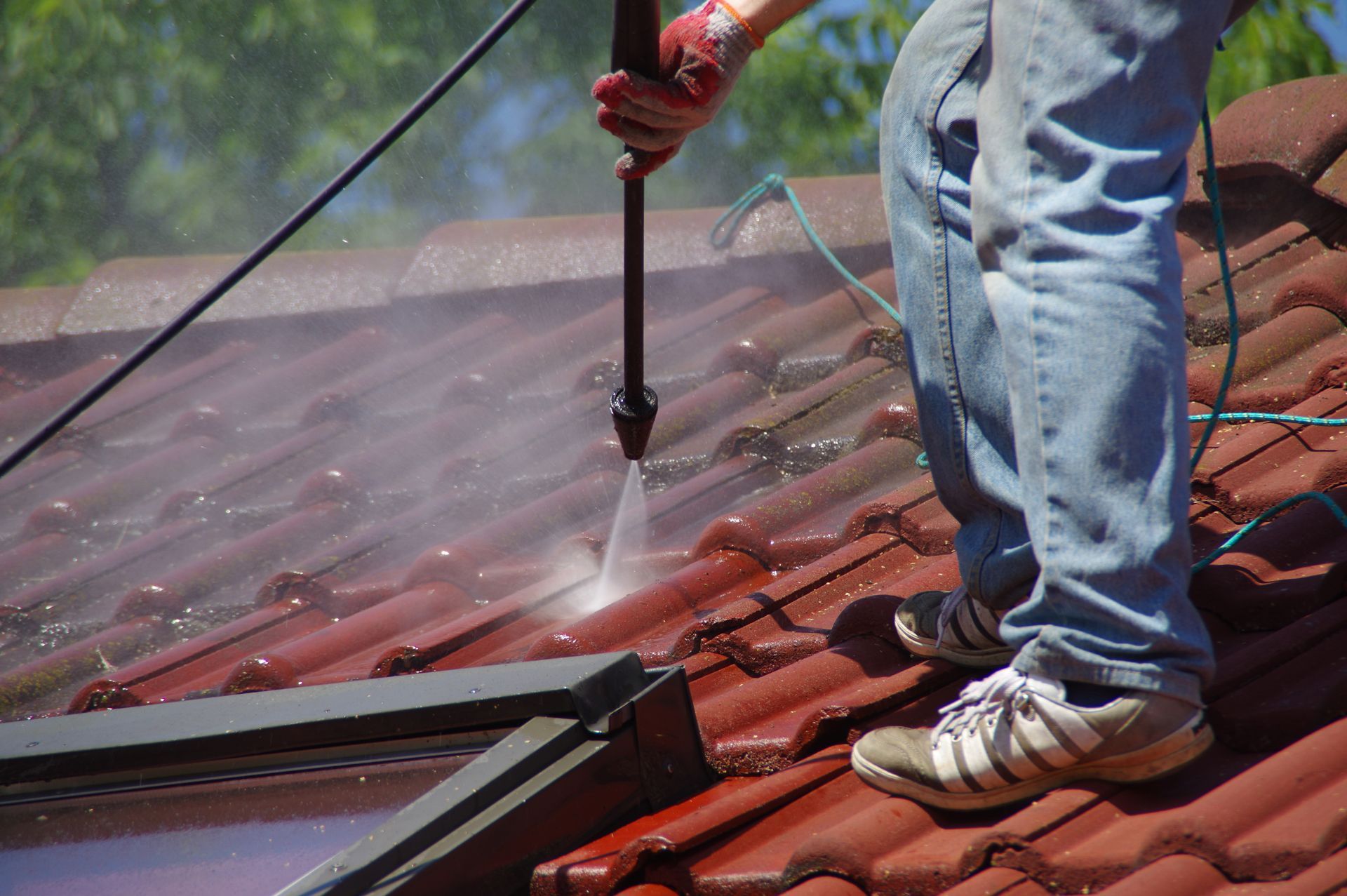 Person pressure washing a red tile roof.