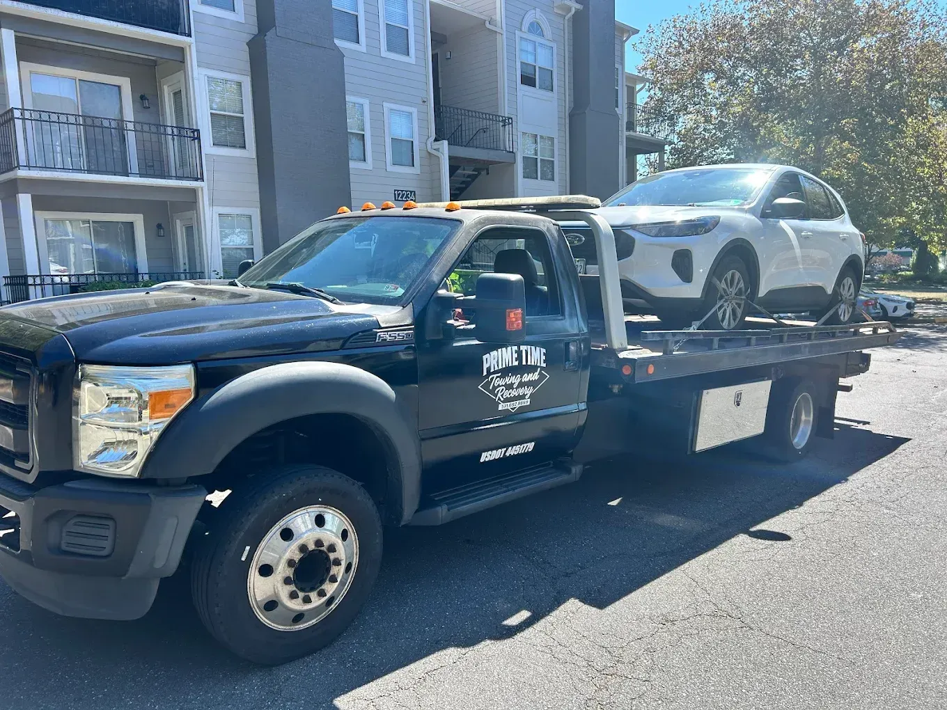 Tow truck hauling a white car on a flatbed in front of apartment buildings