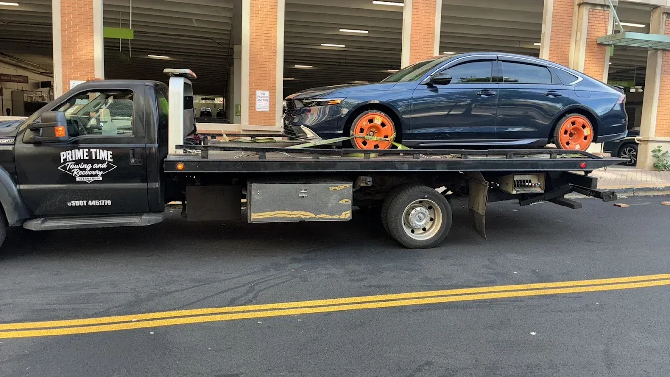 Tow truck hauling a dark blue sports car with orange wheels on a city street