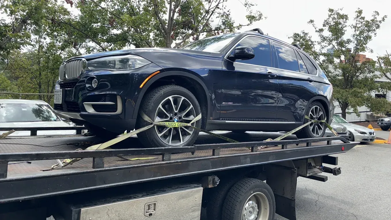 Black SUV strapped on a flatbed tow truck in a parking lot