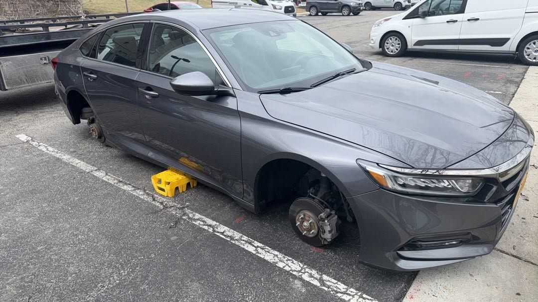 Gray sedan parked in a lot with a wheel removed and a yellow wheel chock underneath