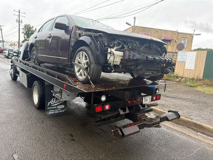 Damaged black car on a tow truck in the rain on a roadside