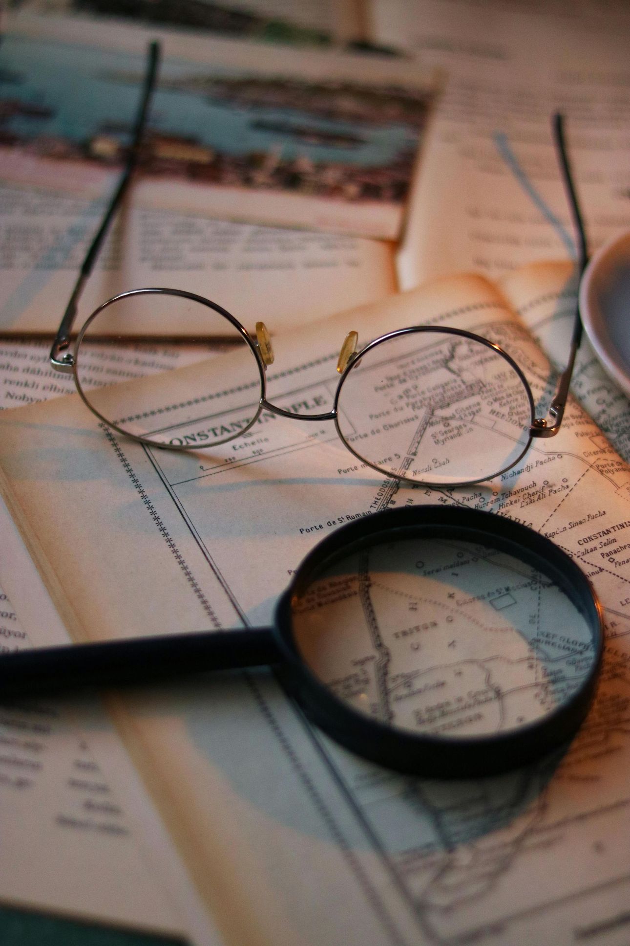 Round eyeglasses and a magnifying glass rest on a vintage map, suggesting exploration or investigation.