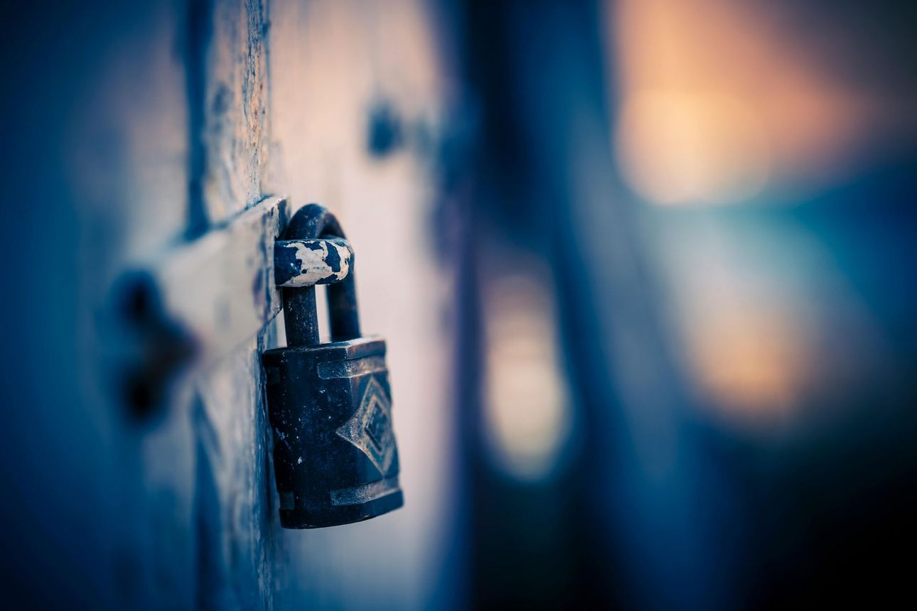 Close-up of a weathered, locked padlock on a blue wooden surface.