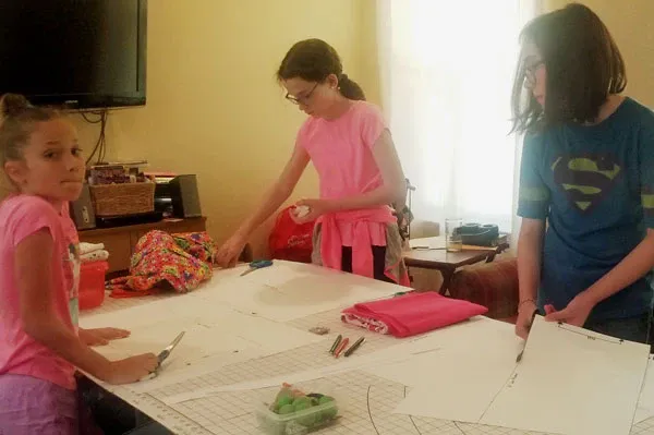 A group of children are sitting around a table cutting fabric.