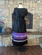 A black dress with a purple skirt is on a mannequin in front of a fireplace.