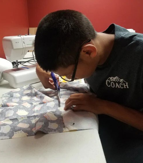 A boy wearing a coach shirt is cutting a piece of fabric