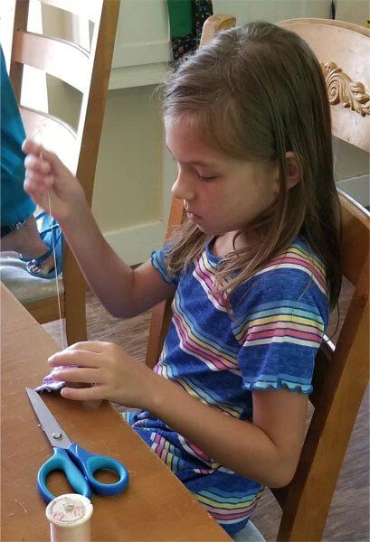 A little girl is sitting at a table with scissors and thread