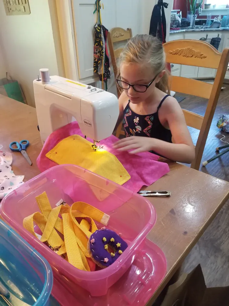 A little girl is sitting at a table using a sewing machine.