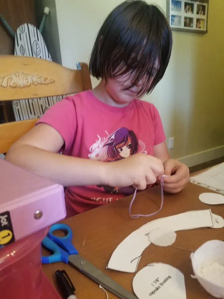 A girl in a pink shirt is sitting at a table with scissors