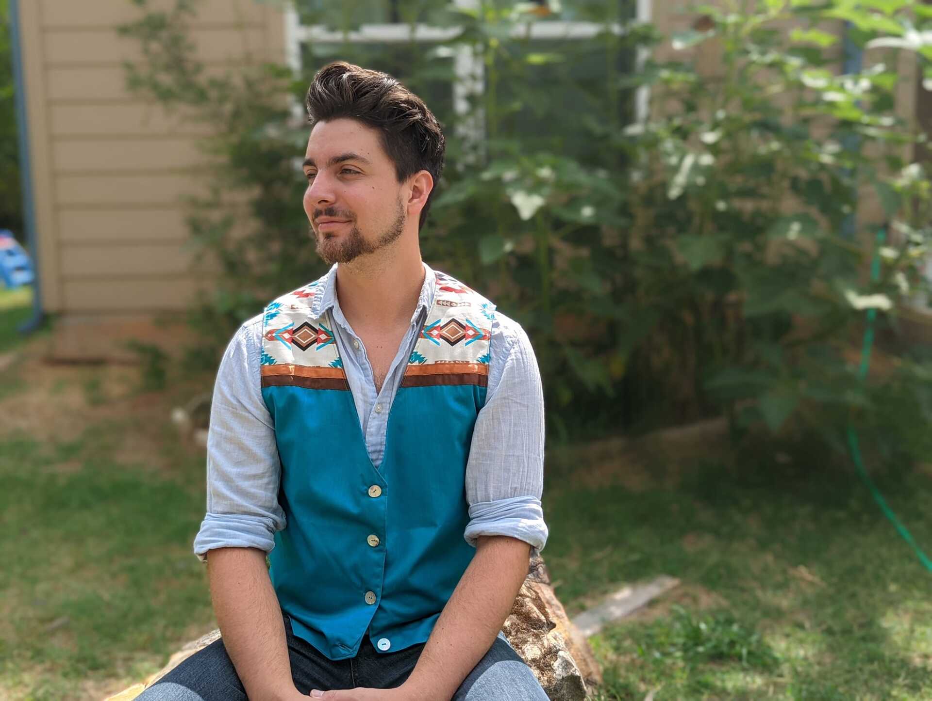 A man in a vest is sitting on a rock in the grass.
