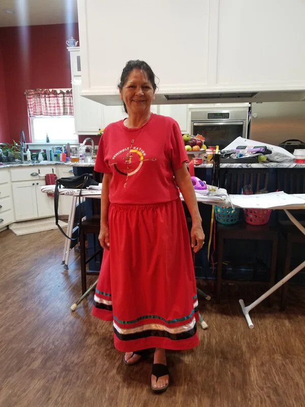 A woman wearing a red skirt and a red shirt which she made during a sewing class and is standing in a kitchen.