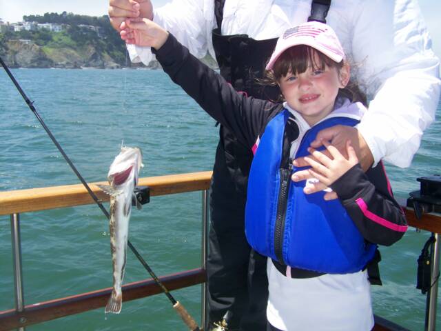 A little girl wearing a life vest is holding a fish