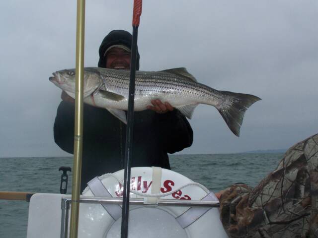 A man holding a large fish in front of a life preserver that says jelly sea