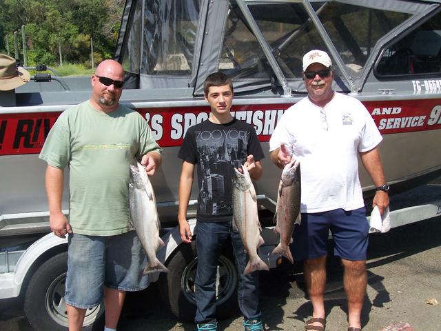 Three men holding fish in front of a boat that says sports fishing