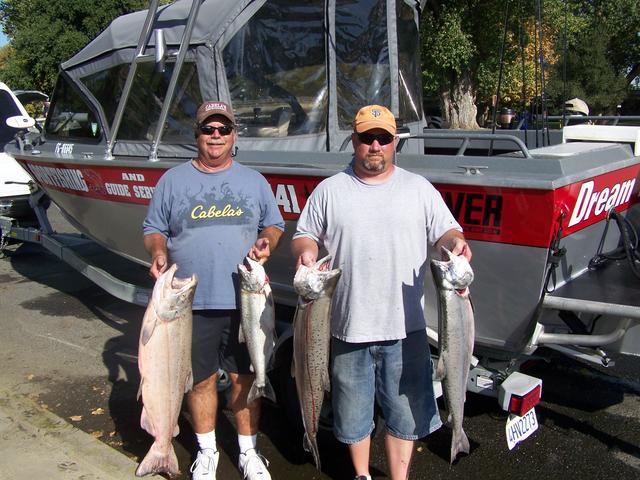 Two men holding fish in front of a boat that says dream
