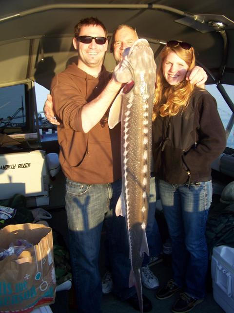 A man and two women holding a large fish in a boat