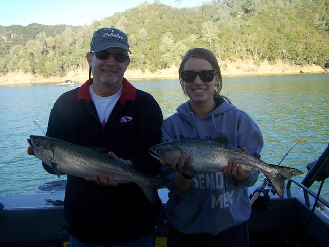 A man and a woman are holding two fish on a boat.