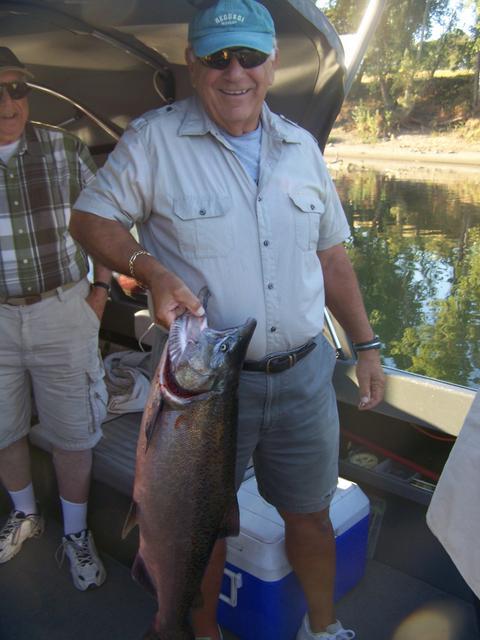 A man holding a large fish next to a blue cooler with the letter t on it