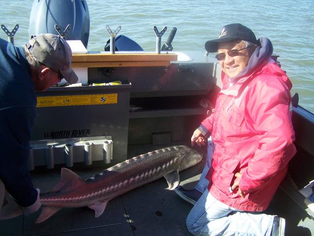 A man in a pink jacket is holding a large fish on a boat