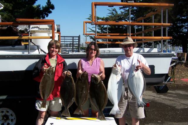 Three people holding fish in front of a boat
