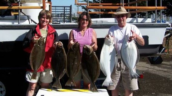 Three people holding up Halibut fish in front of a boat on a dock.