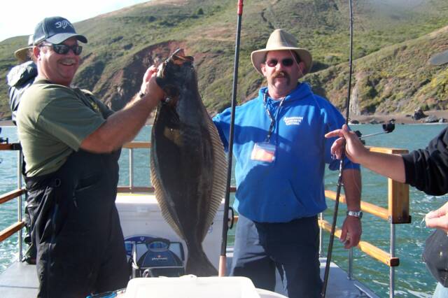 Two men on a boat holding a large fish
