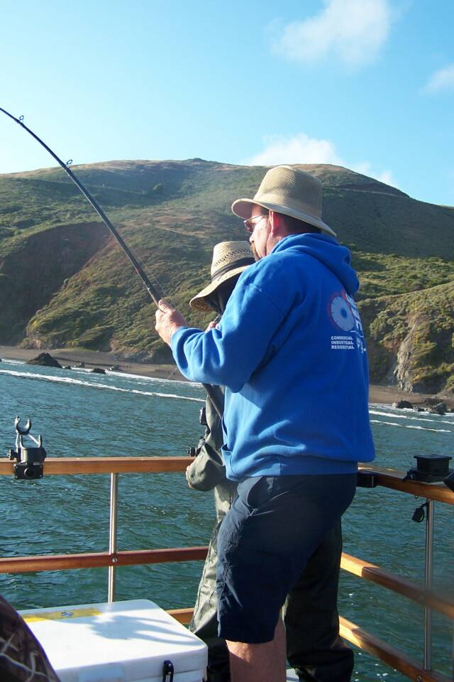 A man in a blue hoodie is fishing on a boat.
