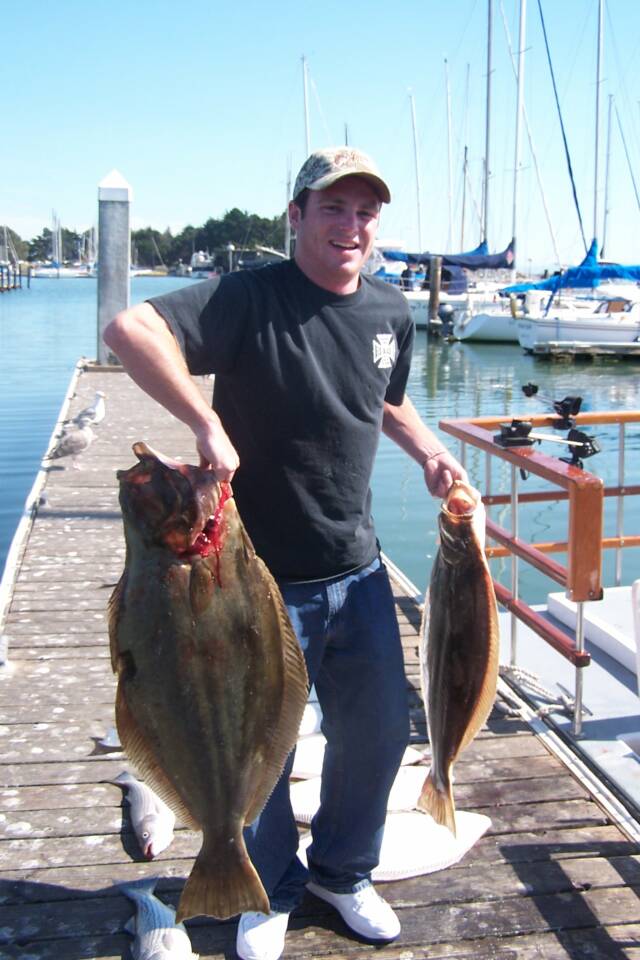 A man is holding two large fish on a dock