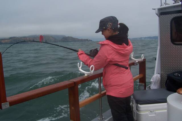 A woman in a pink jacket is fishing on a boat
